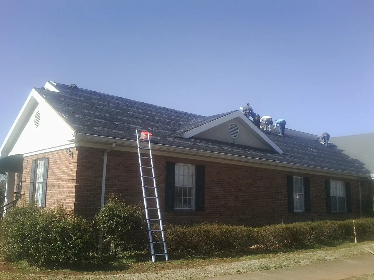 Crew tearing shingles off a brick ranch roof with a ladder set — Emergency Roof Repair work by our crew in Elizabethtown