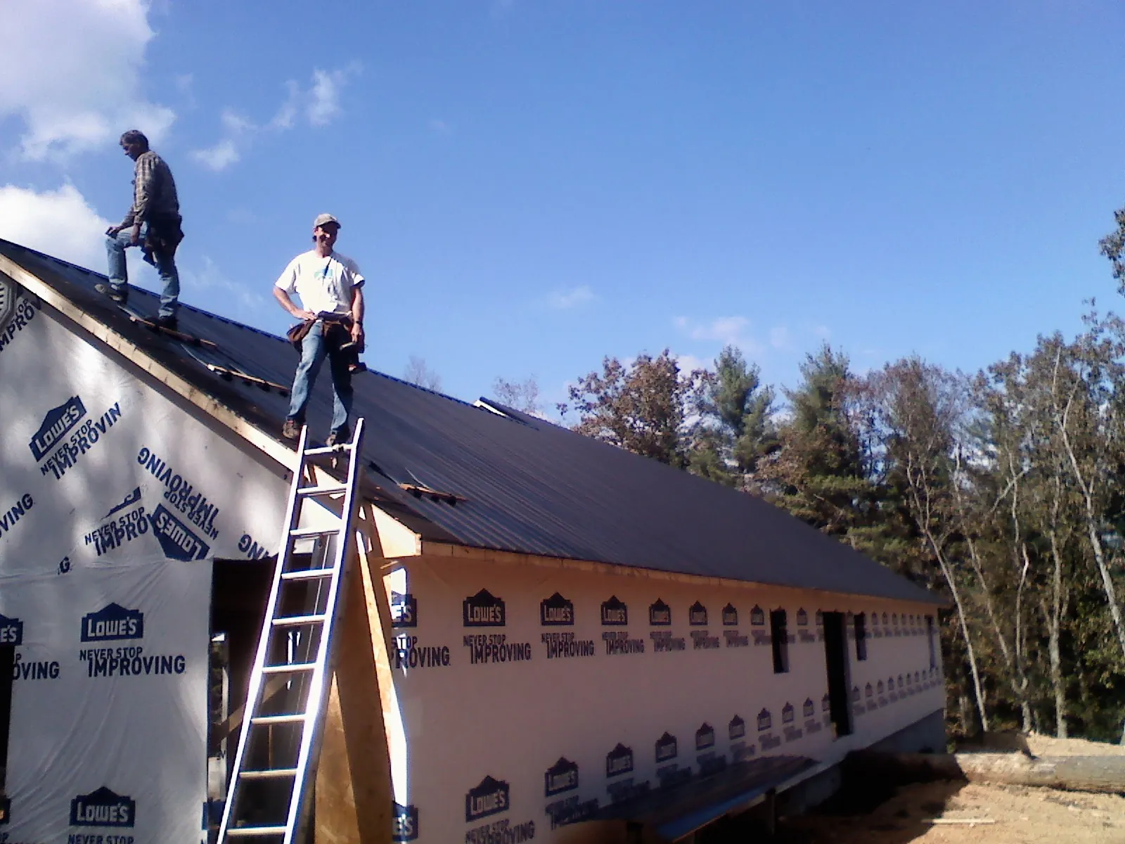 Two roofers standing on a long dark metal roof over a wrapped building in Elizabethtown